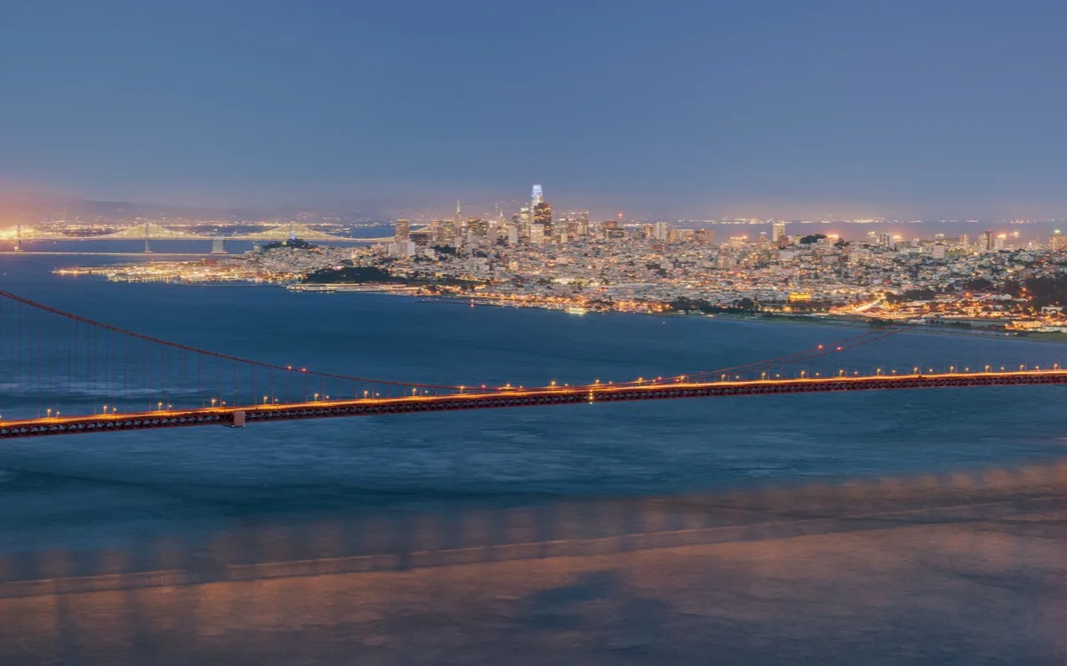 The illuminated Golden Gate Bridge with the San Francisco skyline behind it, from Hawk Hill at blue hour